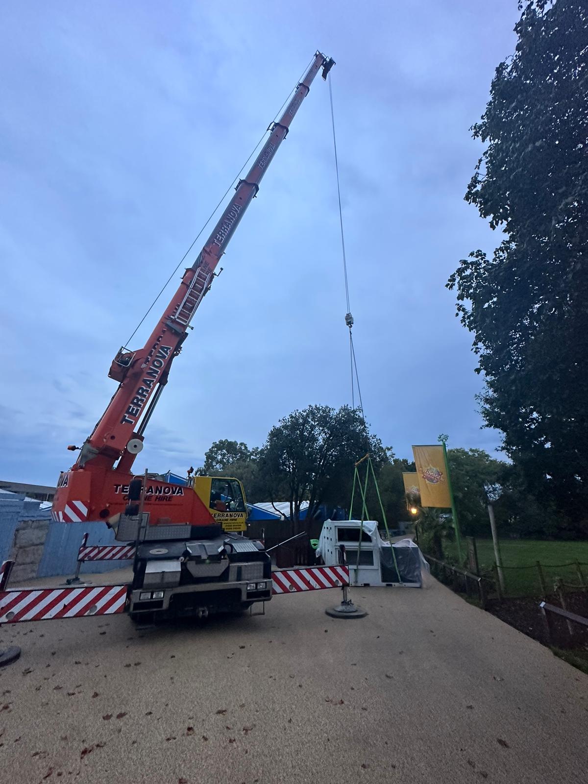 A City Crane on a building site extended vertically to a great height, all set up to transport. It is attached to a load on the ground of building materials, ready to be put to use.