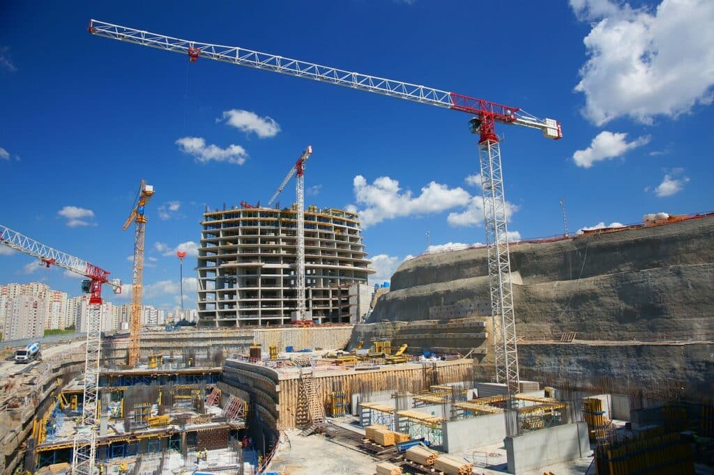 building site with a tower crane and incomplete buildings with scaffolding. The sky is cloudy and blue.