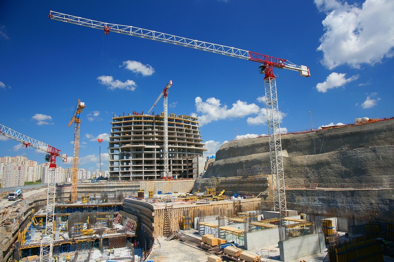 building site with a tower crane and incomplete buildings with scaffolding. The sky is cloudy and blue.